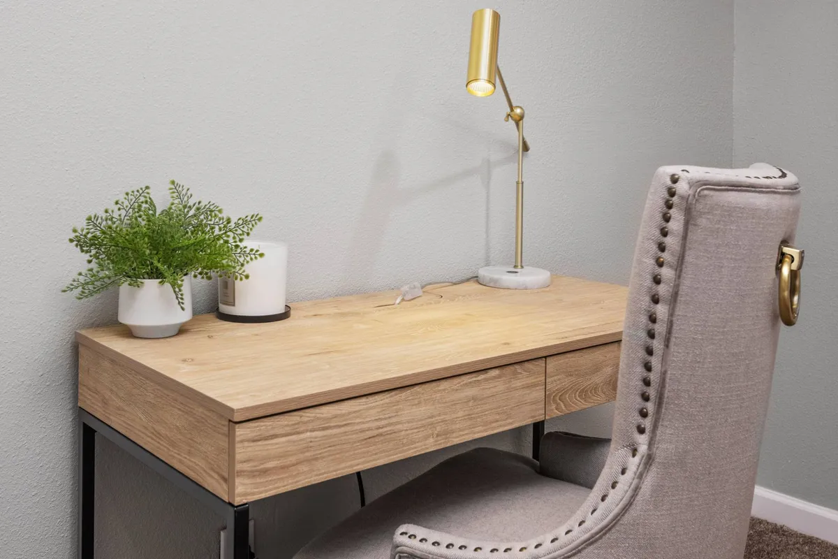 A dedicated workspace with a wooden desk, gold desk lamp, soft chair, potted plant, and candles. The area feels both productive and serene, inviting focused work or creative pursuits in a quiet environment.