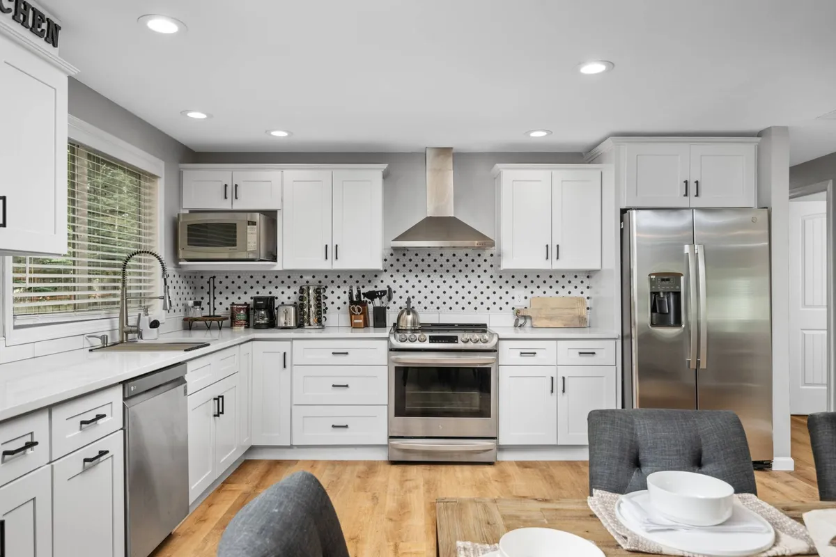 A modern kitchen and dining area with stainless steel appliances, white cabinetry, a polka dot backsplash, and a dining table set with tableware. The space radiates a welcoming and modern vibe, ideal for family meals and gatherings.