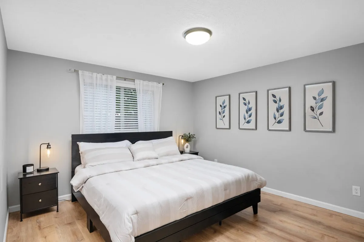 A serene bedroom scene with a neatly made bed, soft sheets, decorative wall art, and a nightstand. The space is inviting and designed for ultimate relaxation.