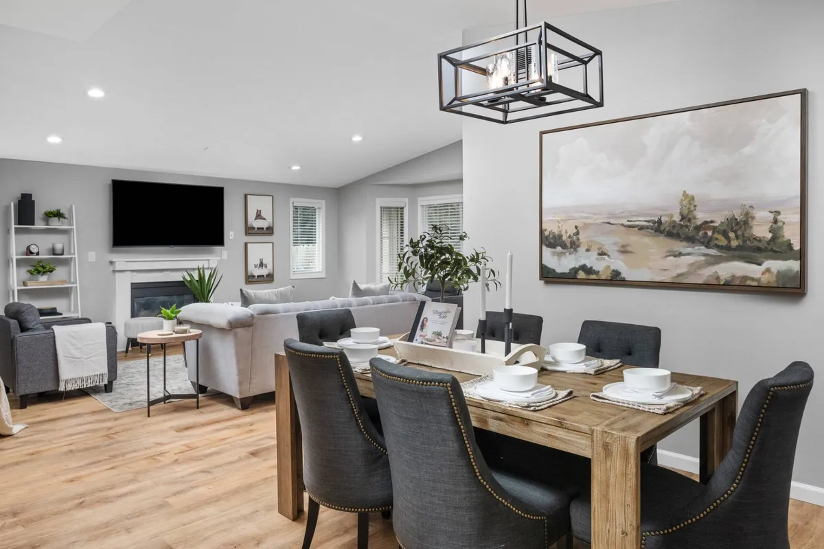 The image showcases a bright, open-concept living and dining area featuring a modern dining table, vibrant artwork on the wall, a cozy fireplace, and a plush sofa. The scene radiates warmth and invites guests to gather for shared meals, relax with a book, or enjoy meaningful conversations.