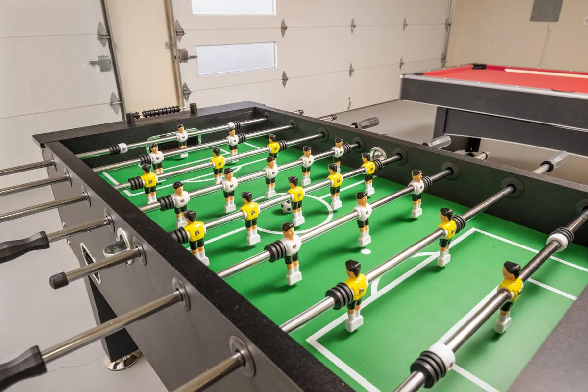 A bright interior shot focused on the energetic atmosphere of the game room, with both a foosball table and a pool table at the center. The setup suggests active use and is surrounded by space for movement and interaction, perfect for competitions and group gatherings.