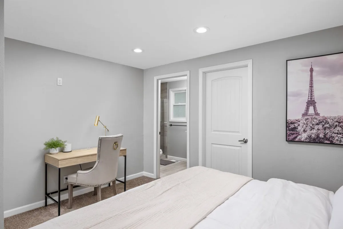 A calm and productive setting with a bed and an adjacent desk with a chair, complemented by tasteful Eiffel Tower artwork on the wall. The room is well-lit and designed for both relaxation and efficient work.