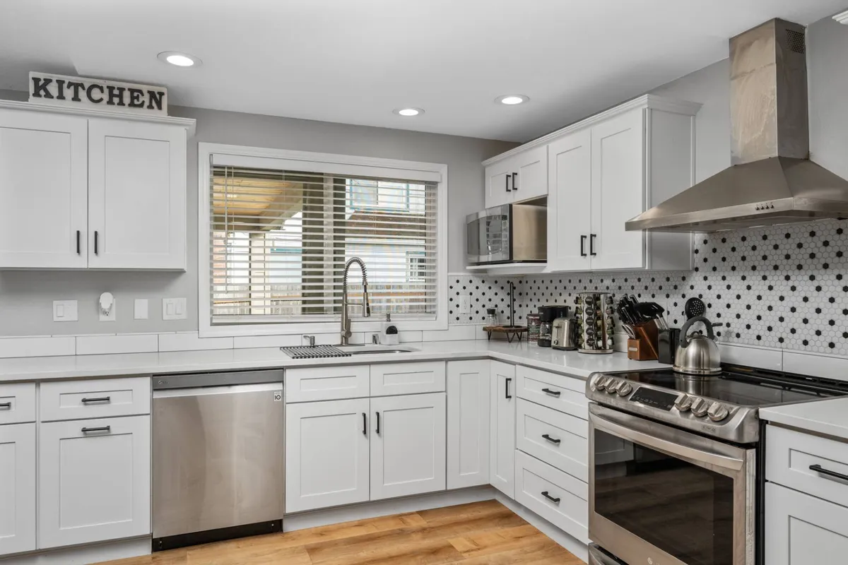 A modern kitchen with sleek white cabinetry, stainless steel appliances, and a large window letting in natural light. The layout is ideal for group meal prep and conversation, emphasizing the home's suitability for socializing and entertaining before venturing out to local restaurants.