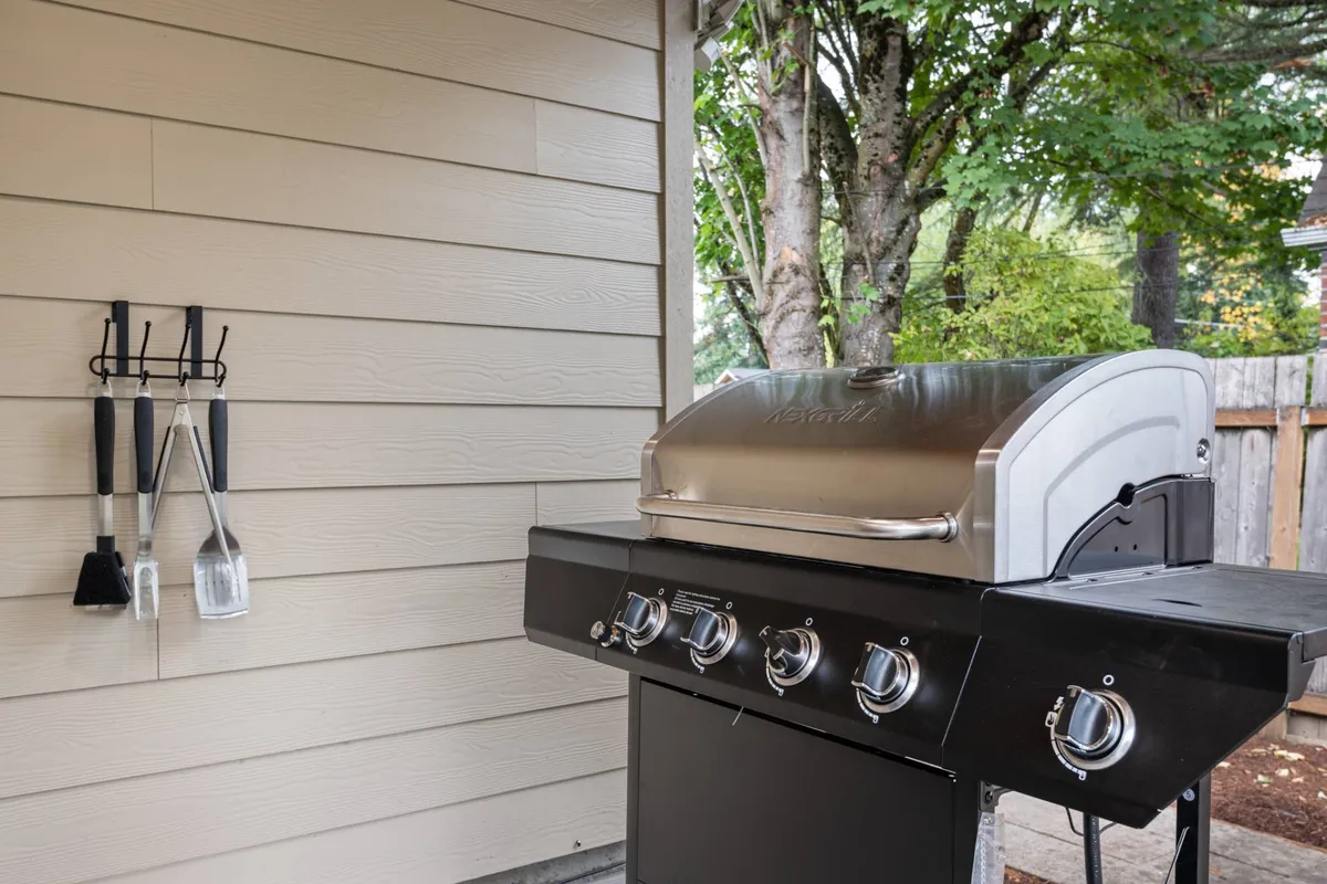 Focusing on a well-equipped patio with a modern grill and utensils, this image emphasizes the possibilities for al fresco dining and barbecues. The covered portion of the patio is highlighted, suggesting year-round usability regardless of the Pacific Northwest weather. The scene is casual and social, supporting activities like dining and gatherings.