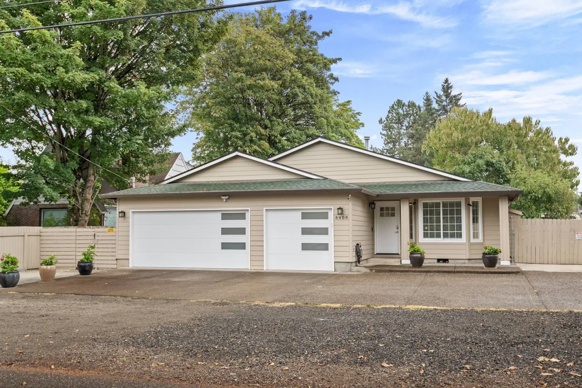 A view of the home’s exterior from a slightly different angle, highlighting modern garage doors, a cozy front porch, and green trees in the yard. The setting suggests both relaxation and socialization, with hints of backyard gatherings and outdoor relaxation.